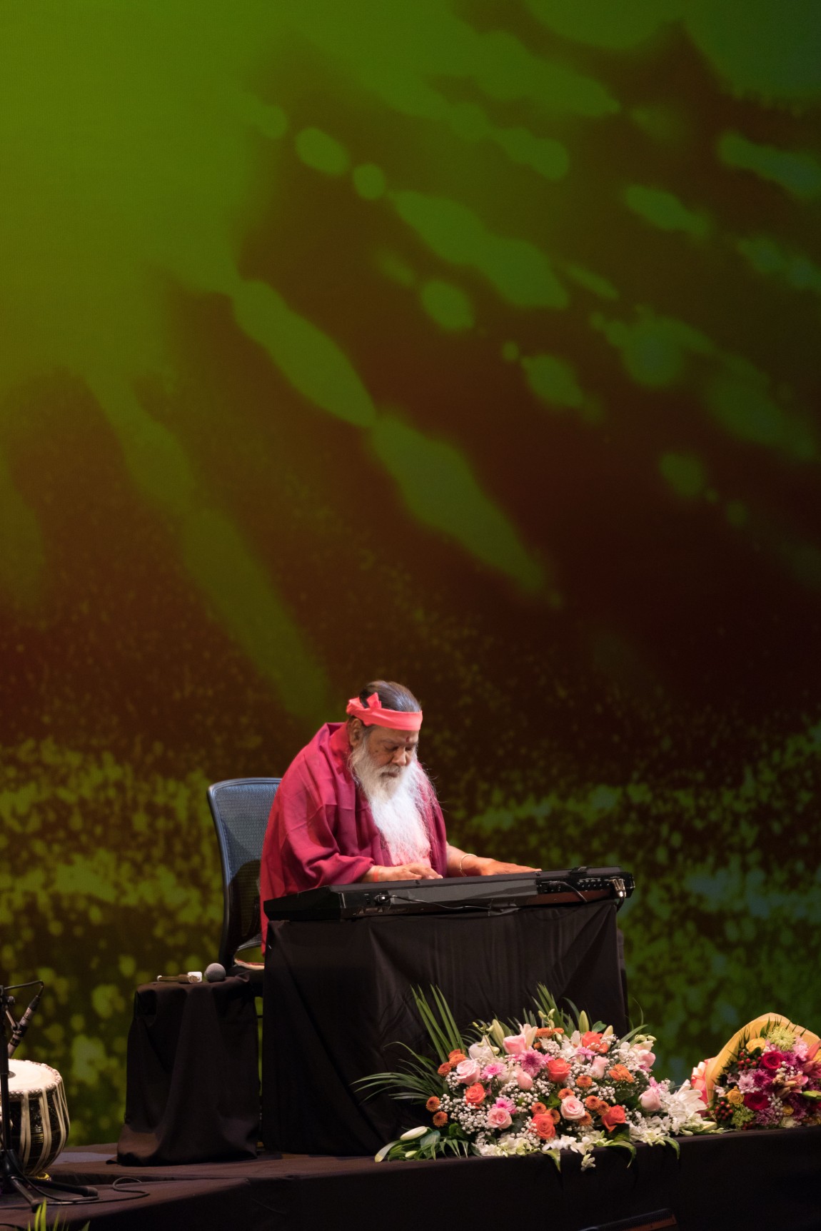 Sri Swamiji at keyboard — green light backdrop